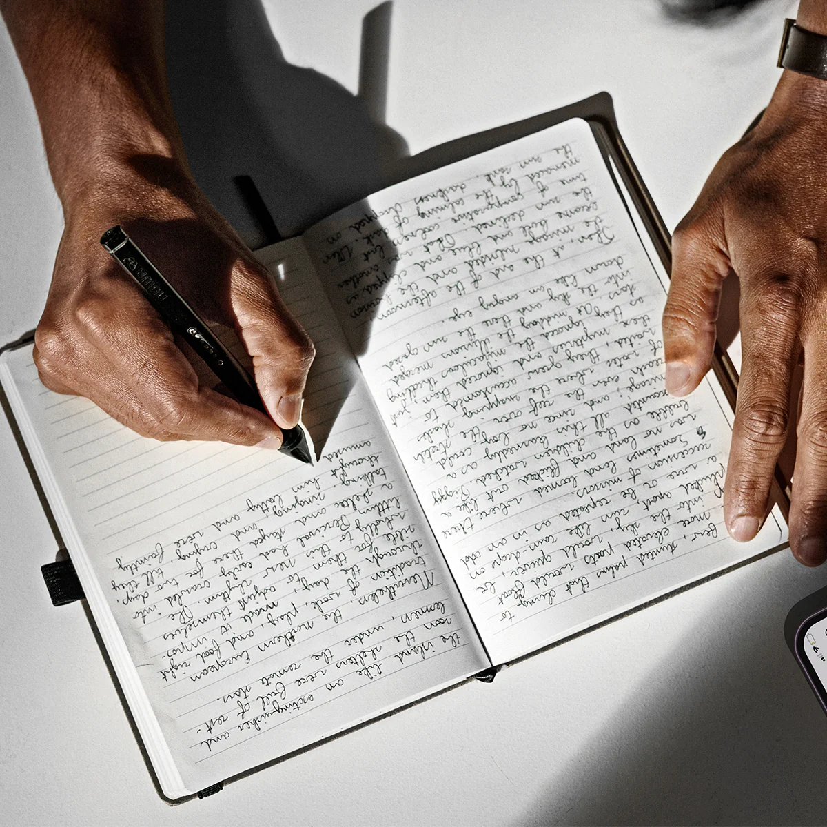 A person writing in a notebook with the Newa Pen